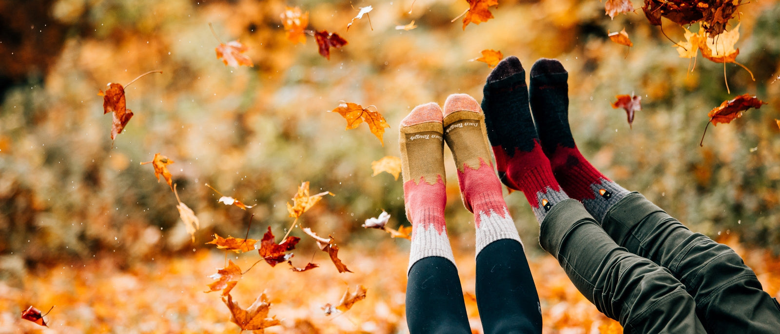 Two pairs of feet in Darn Tough wool hiking socks kick up through a shower of autumn leaves in Vermont.