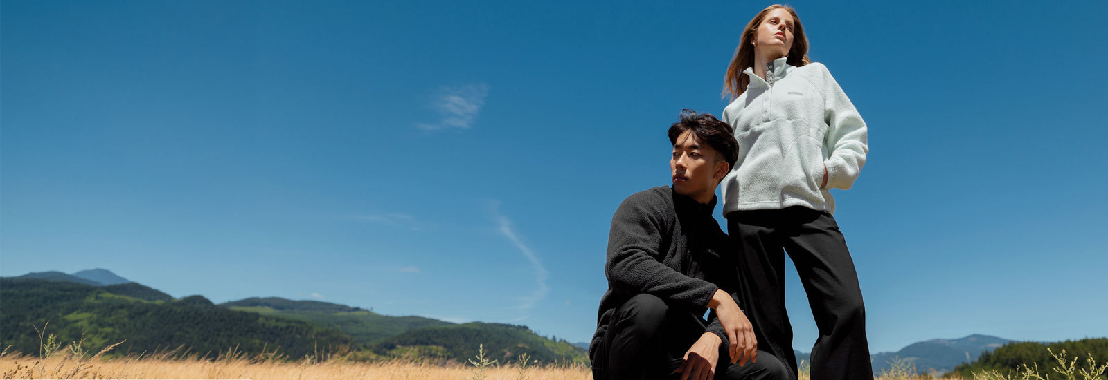 Two people wearing Columbia fleeces in a sunny mountain landscape with dry grass and hills.