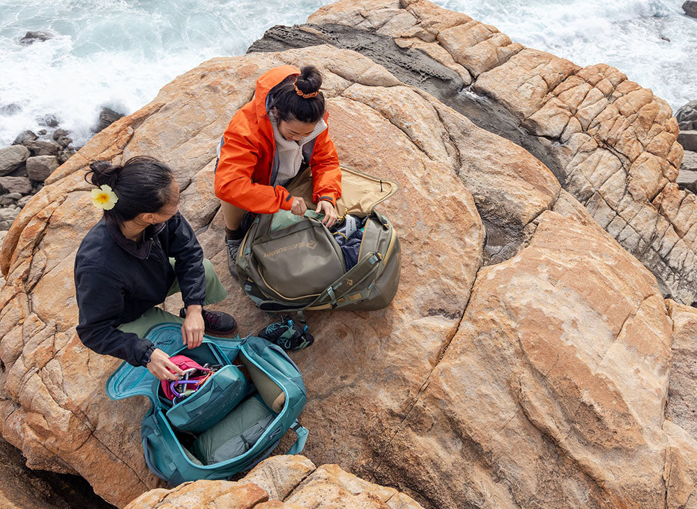 Two people packing Sea to Summit bags on a rocky coastal outcrop by the sea.