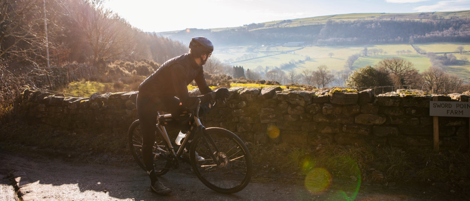 man stops to take in a view over a low brick wall as he straddles a bicycle