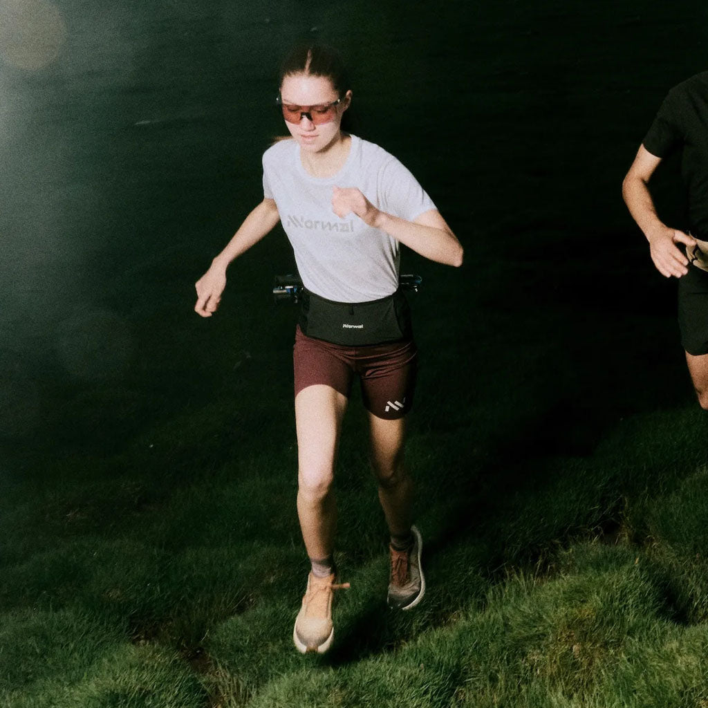 A runner wearing Norma women's gear trails running at night with a headlamp and waist belt.
