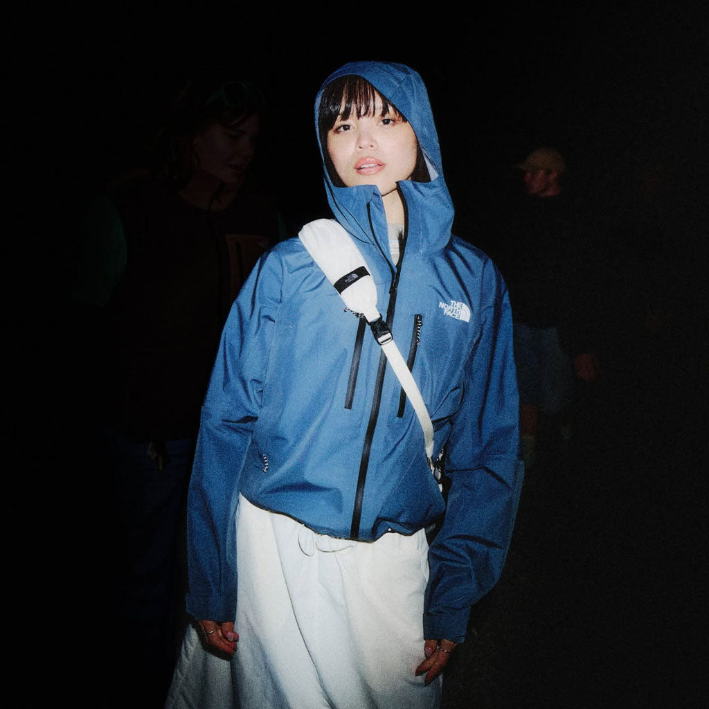 Person wearing The North Face blue hooded jacket with white shoulder bag against dark background